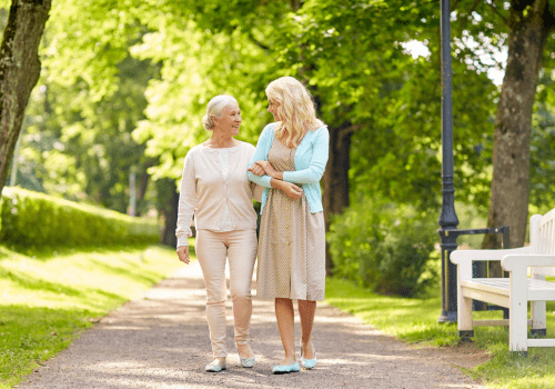 Eine Frau geht mit ihrer älteren Mutter im Park einer Seniorenresidenz spazieren